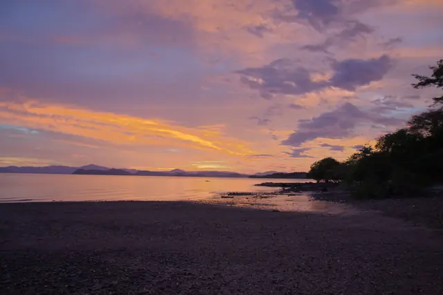 Sunset over a calm gulf with the hills of a peninsula on the horizon