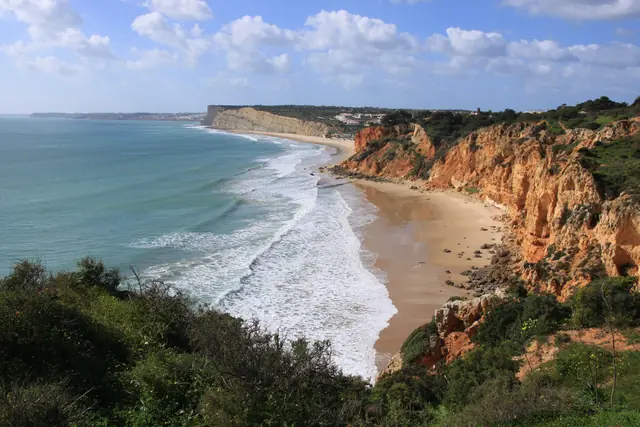 Ochre sea cliffs above a long beach and surf